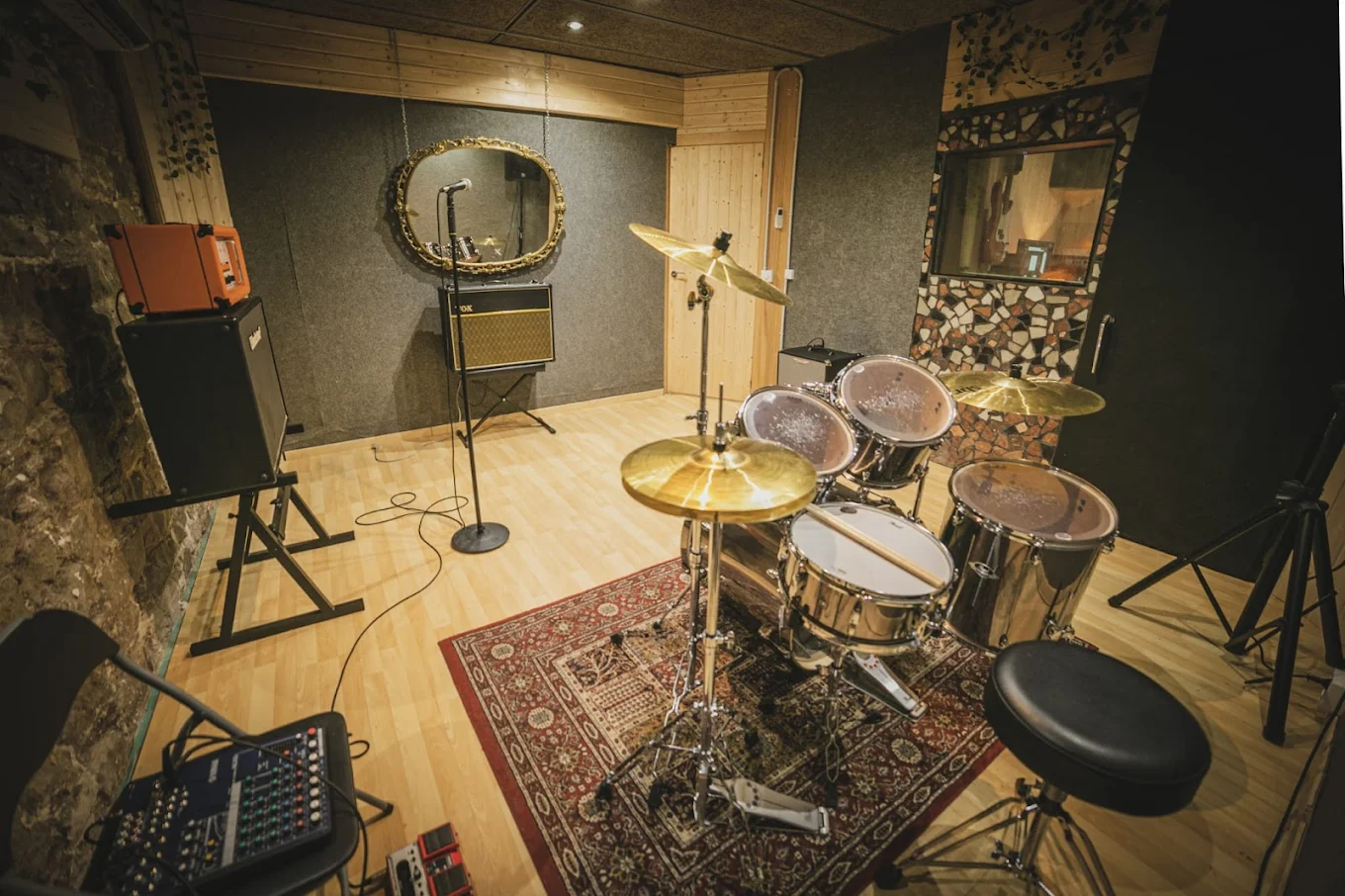 Sala tratada acústicamente con bateria preparada, dos amplificadores y ventana con cristal a la sala de control.